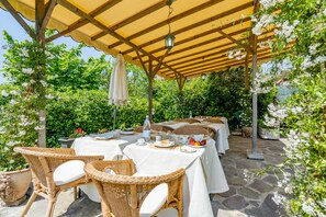 An outdoor dining area with wicker chairs and tables covered with white tablecloths, surrounded by greenery and stone flooring. - B&B Miami Beach (Pietrasanta)
