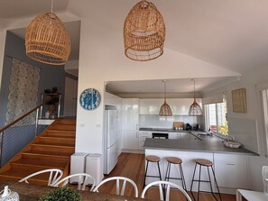 A modern kitchen with white cabinets, a central island with stools, and hanging wicker light fixtures. - Beach House for Family or Couples with views & 2 minute walk to beach and shops (Copacabana)