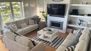 Ein modernes Wohnzimmer mit zwei beigen Sofas, einem Couchtisch, einem Kamin und einem darüber montierten Fernseher.