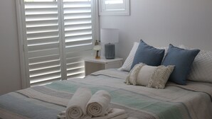 Ein ordentlich bezogenes Bett mit aufgerollten Handtüchern, einer Nachttischlampe und einem Nachttisch mit einer Vase.