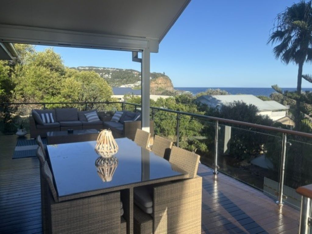 A covered outdoor seating area with a table and chairs, overlooking a coastal landscape.