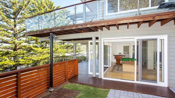 Ein modernes Haus mit einer Holterrasse, einem gläsernen Balkon und einem Billardtisch, der durch die Glastüren sichtbar ist.
