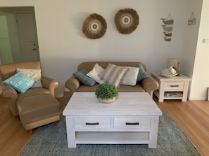 Ein Wohnzimmer mit einem beigefarbenen Sofa, einem weißen Couchtisch und einem kleinen Beistelltisch mit einer Lampe.