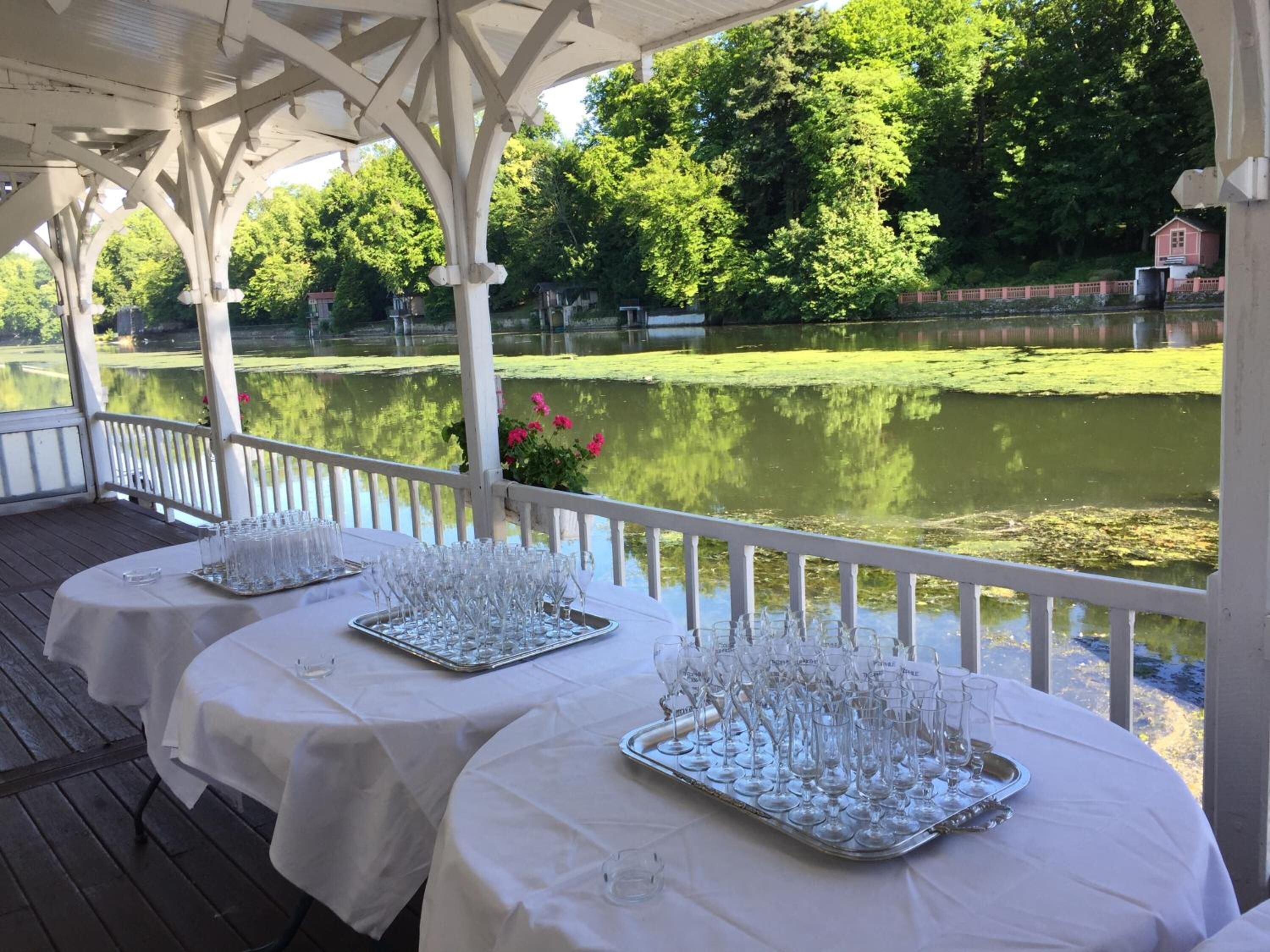 Een overdekt buitengebied met tafels, ingericht voor een bijeenkomst, met uitzicht op water en groen.