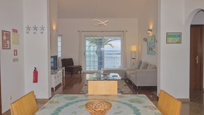 Un vaste espace de vie comprenant une table à manger, un canapé et offrant une vue sur la mer grâce à de grandes fenêtres.