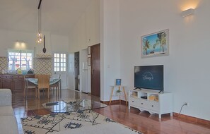 Ein geräumiges Wohnzimmer mit einem Glastisch, einem Flachbildfernseher und einem Essbereich mit Stühlen und Tisch.
