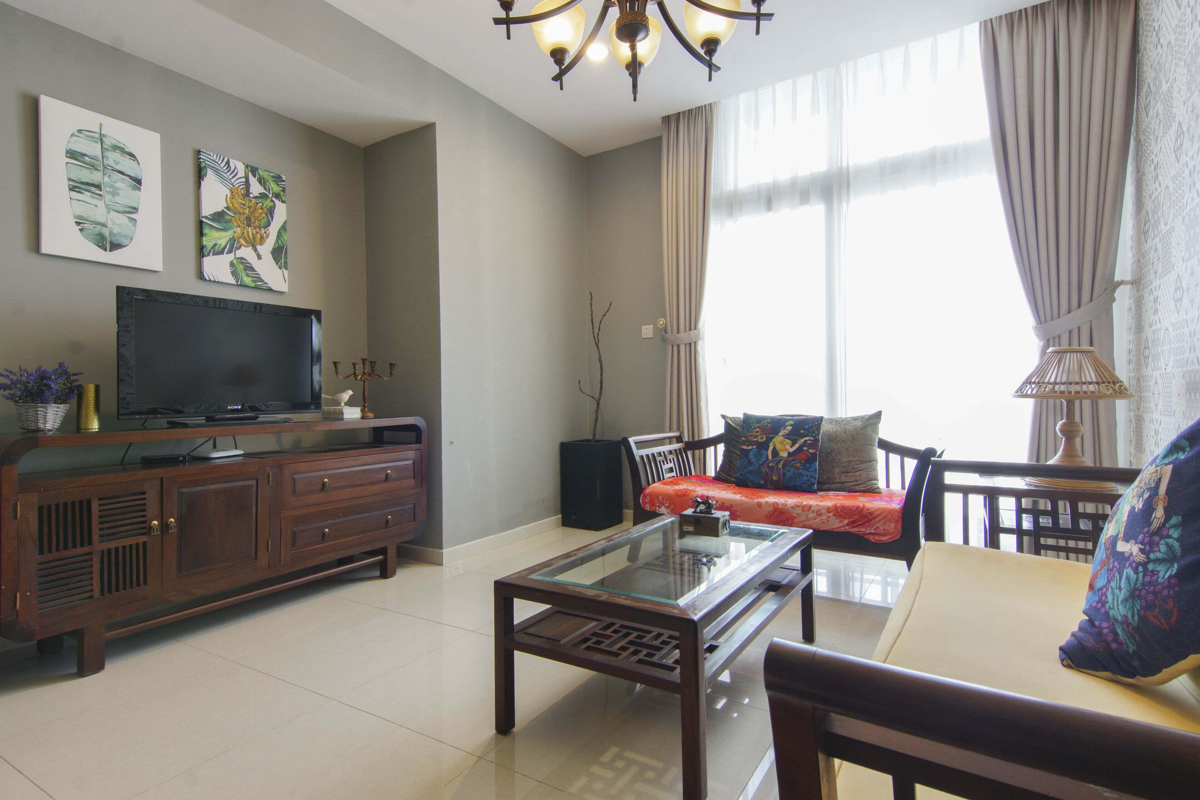 A living room with a TV on a wooden cabinet, a glass coffee table, a sofa with cushions, and a lamp.