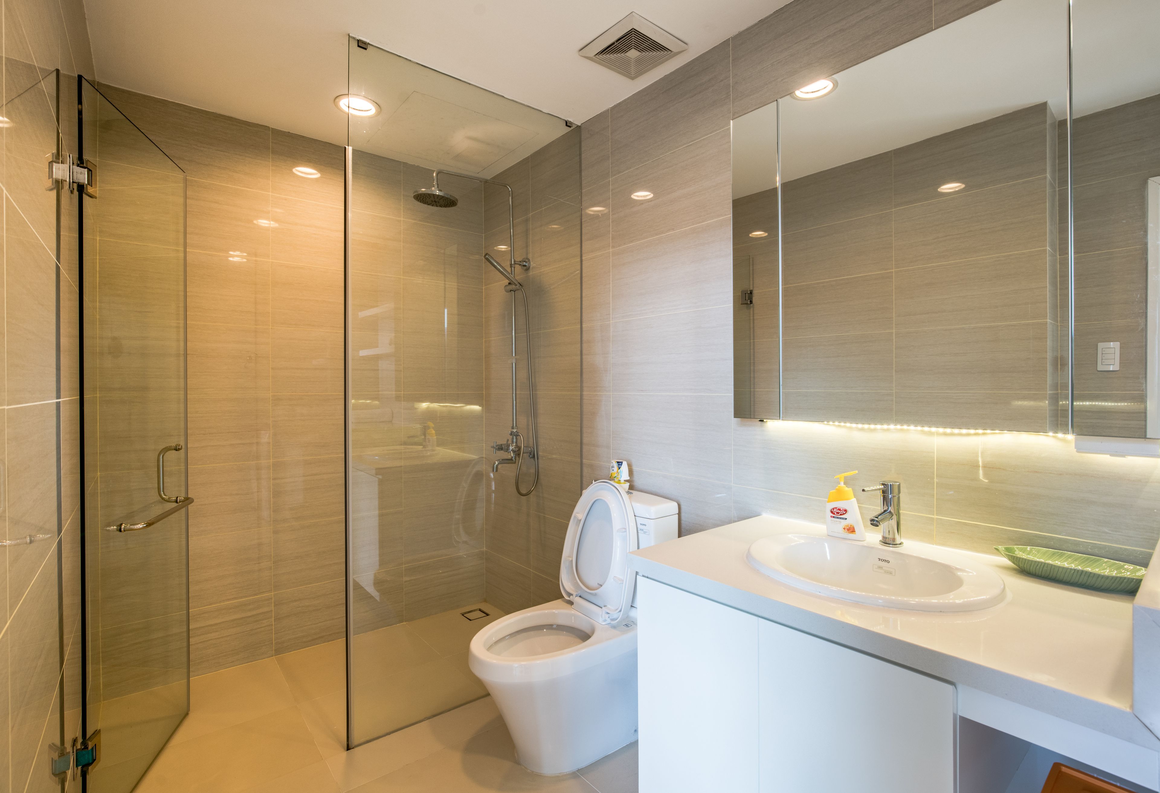A modern bathroom with a glass-enclosed shower, a toilet, and a sink with a mirror above.