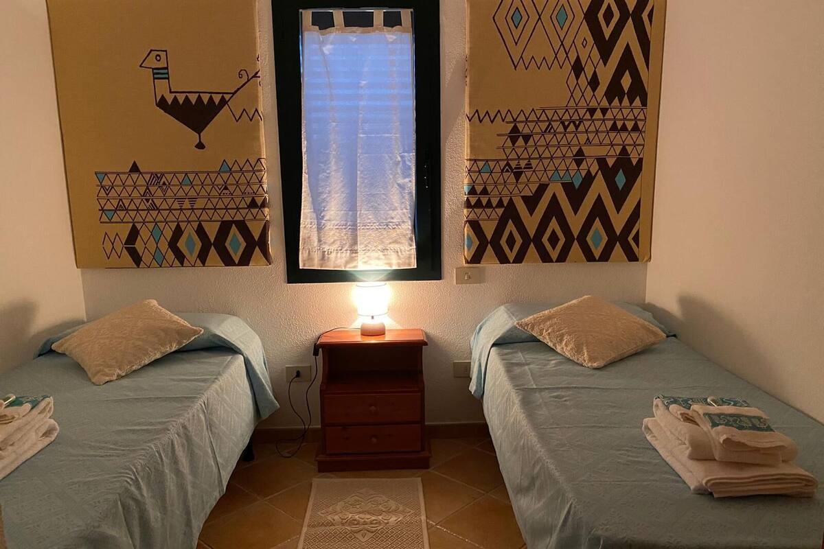 A room with two beds, a nightstand, a lamp, and patterned wall art.