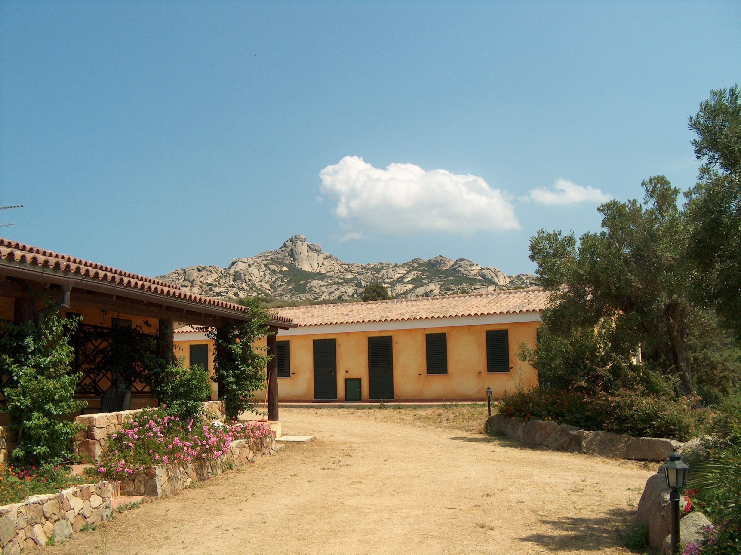 A building with a tiled roof and a stone wall in front. There is a mountain in the background.