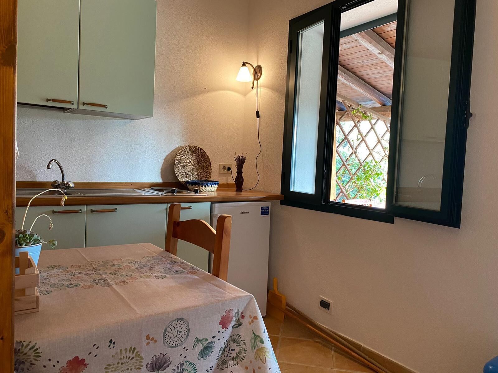 A compact kitchen with a dining table, a small refrigerator, and a window with a view of greenery.