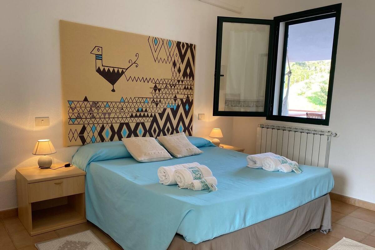 A bedroom with a bed, two bedside tables, a wall art piece, a window, and a radiator.