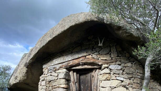 Una cabaña de piedra con puerta de madera, rodeada de vegetación natural.