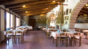 Un comedor amplio con varias mesas y sillas, paredes de piedra y vigas de madera.
