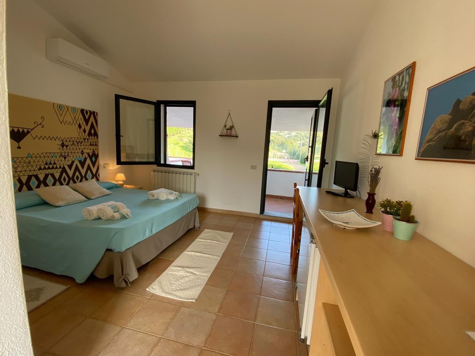 A bedroom with a bed, a desk, a chair, a TV, and a window.