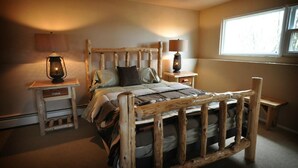 A rustic wooden bed with a headboard, two bedside tables with lamps, and a window providing natural light. - Monster Lake Ranch (Cody)