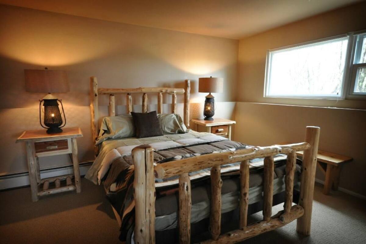 A rustic wooden bed with a headboard, two bedside tables with lamps, and a window providing natural light.