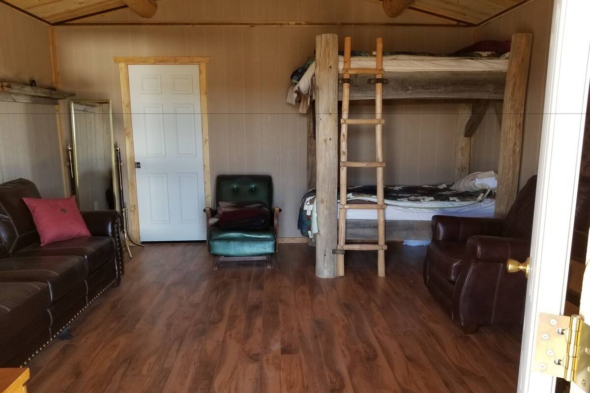 A compact room with a wooden bunk bed, a green armchair, a brown leather sofa, and a door.