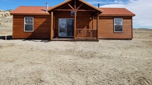 A wooden cabin with a metal roof, a front porch, and a door with a glass panel. - Monster Lake Ranch (Cody)