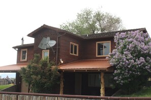 A wooden house with a satellite dish, a porch, and a tree with purple flowers. - Monster Lake Ranch (Cody)