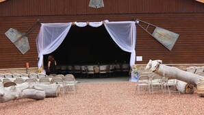 A barn with a stage set up for an event, featuring a white canopy and chairs arranged in rows. - Monster Lake Ranch (Cody)