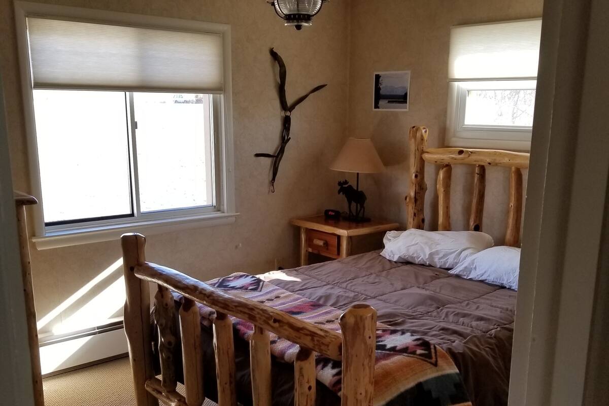 A bedroom with a wooden bed frame, a ceiling fan, a nightstand with a lamp, and a wall-mounted decoration.