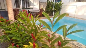 Piscina rodeada por plantas verdes exuberantes e flores vermelhas.