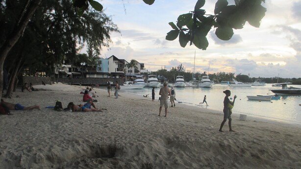 Uma praia com pessoas relaxando e barcos na água.