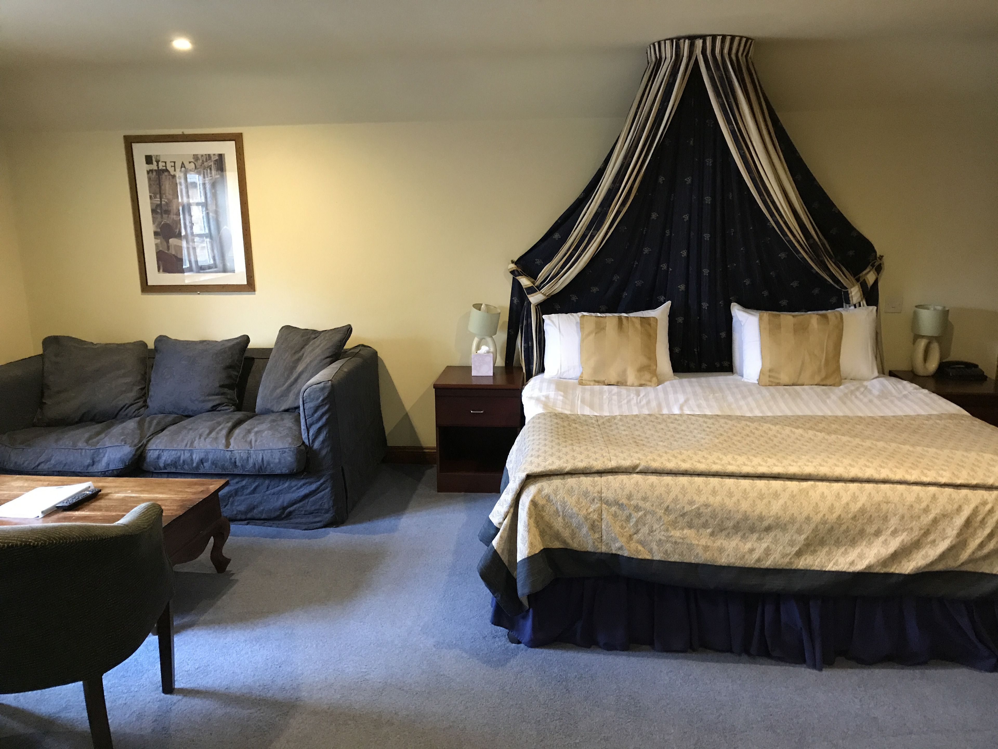 A bedroom with a four-poster bed, a sofa, a bedside table, and a framed picture on the wall.