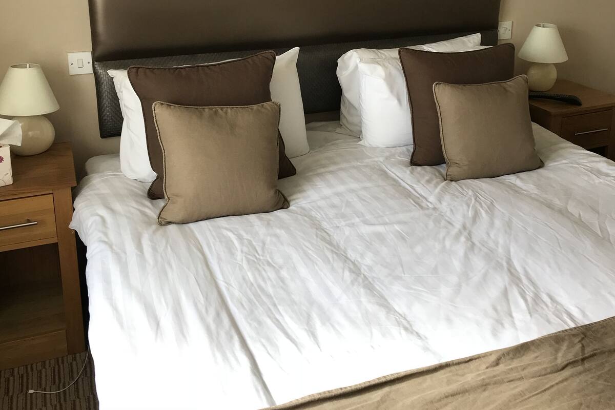 A neatly made bed with white linens and multiple pillows, a dark headboard, and bedside lamps on wooden nightstands.