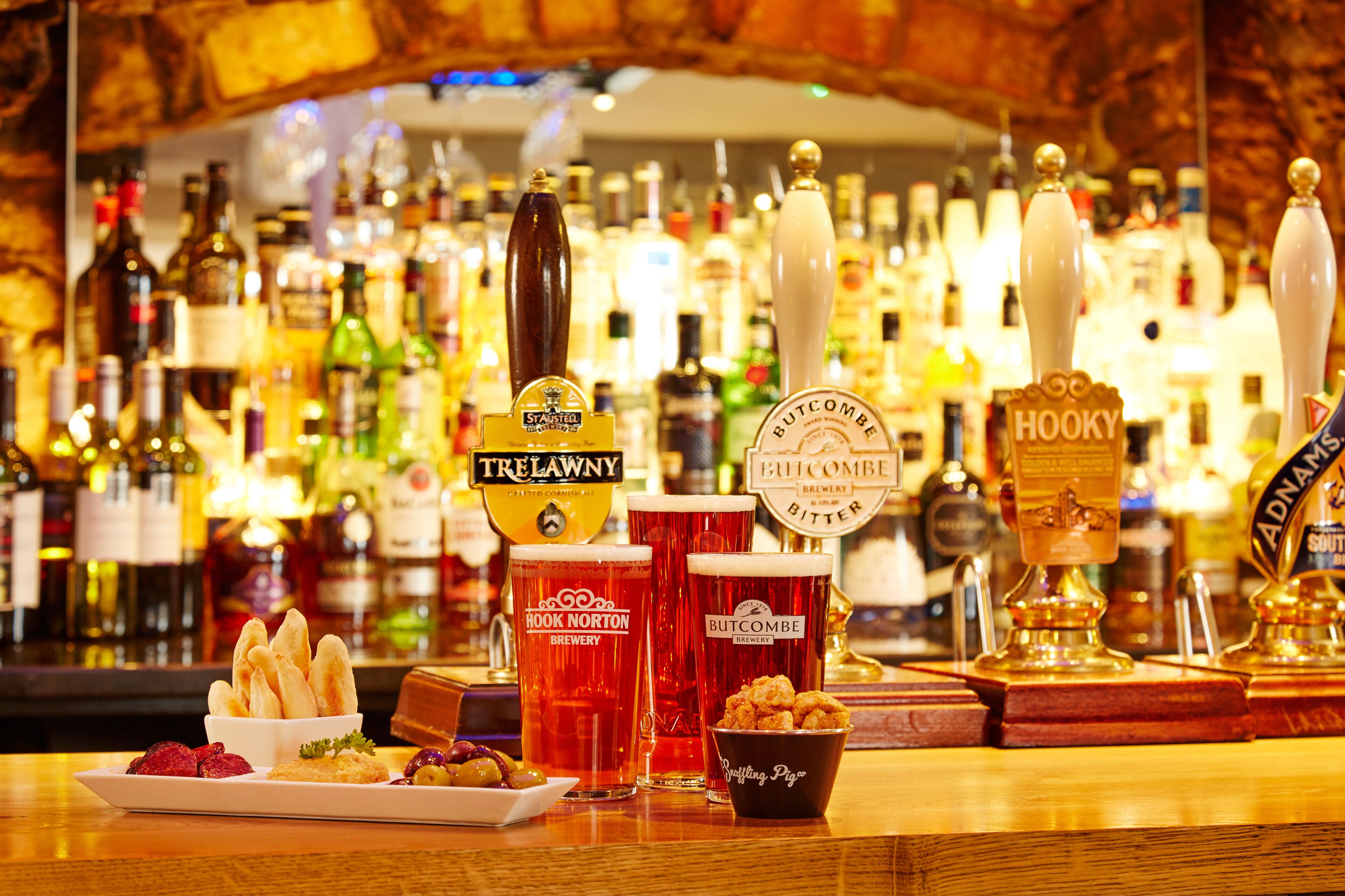A bar with multiple beer taps, glasses of beer, and a variety of bottles in the background.