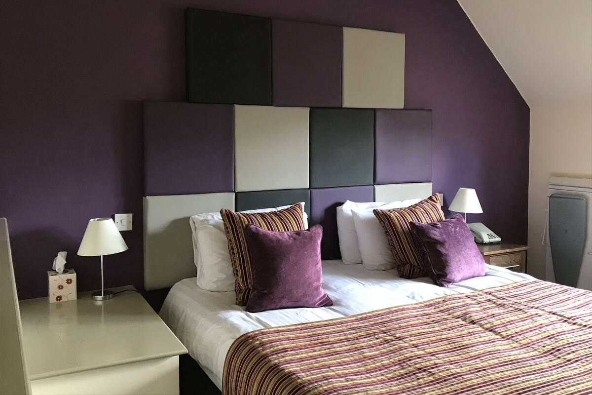 A hotel room with a modern design, featuring a large bed with a striped bedspread, two nightstands with lamps, and a unique geometric headboard.
