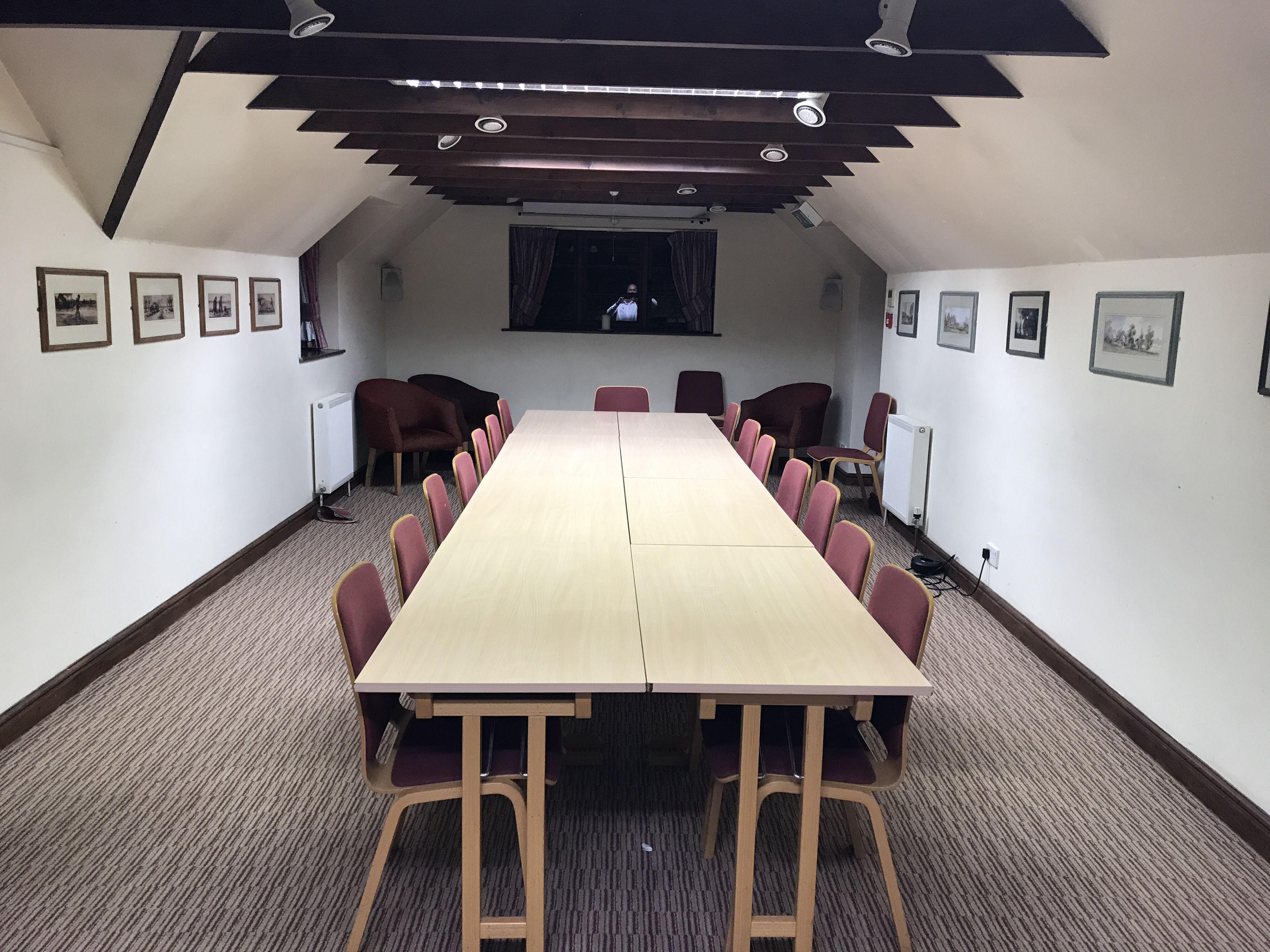 A conference room with a long table and chairs, framed pictures on the walls, and a window with curtains.