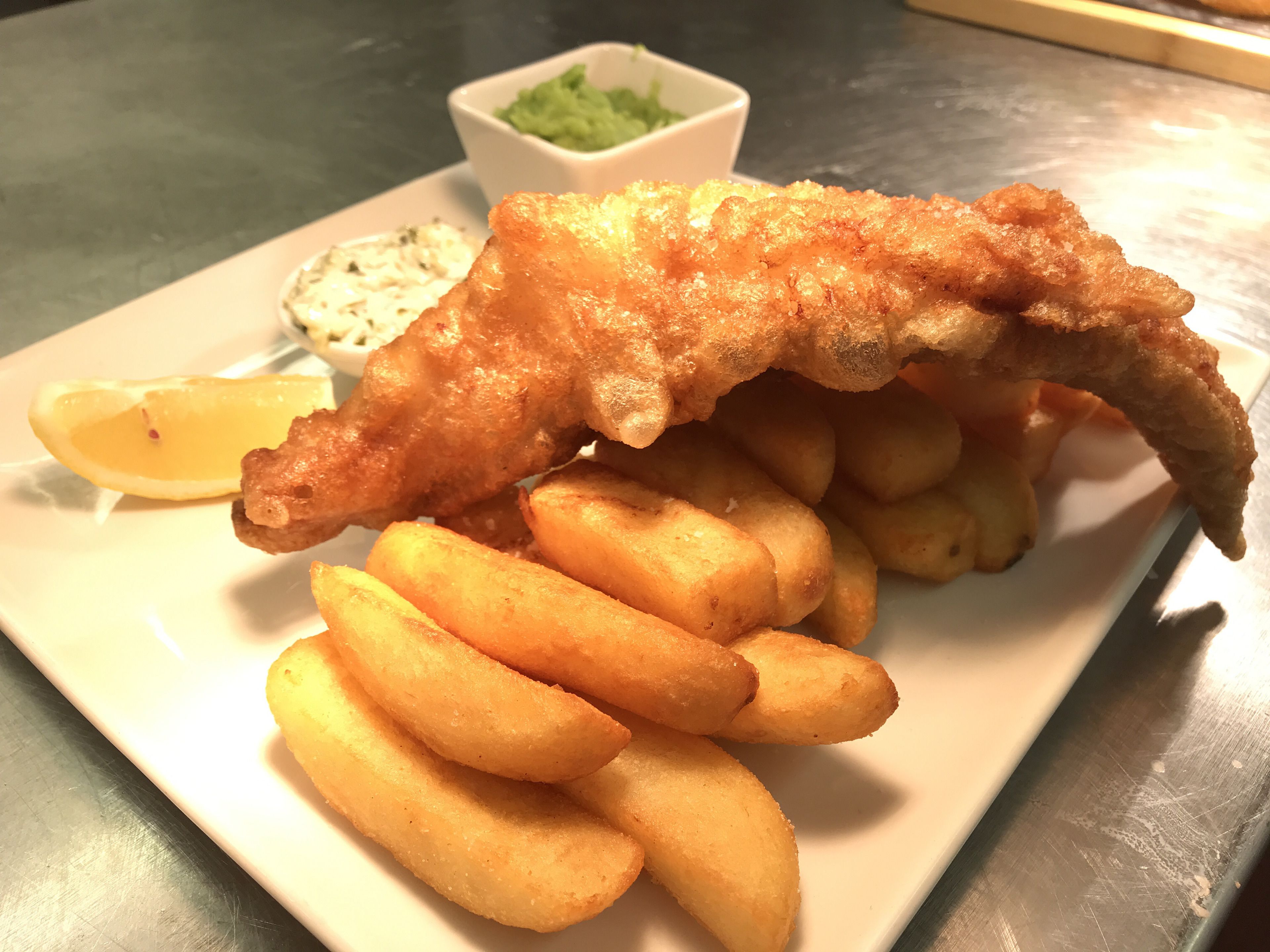 A plate of fish and chips with lemon wedges and a small bowl of tartar sauce.