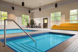 An indoor swimming pool with clear blue water, a metal ladder, and a yellow seating area. - Microtel Inn & Suites By Wyndham Val-d Or (Val-d'Or)