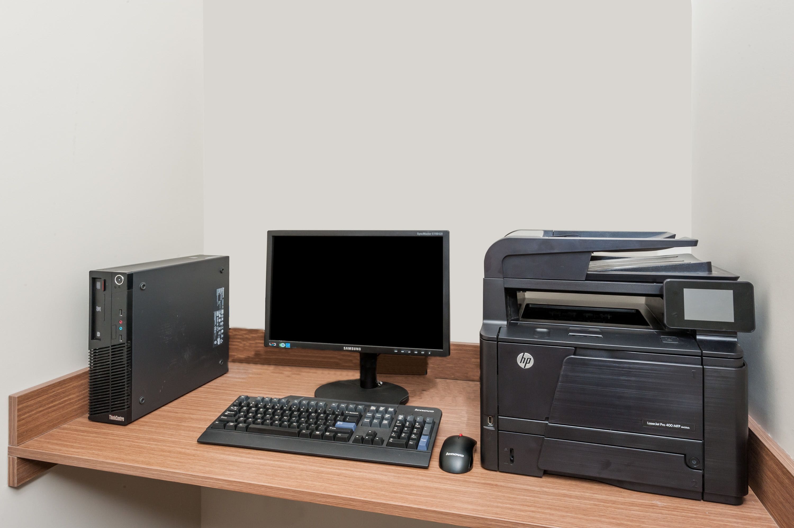 A desktop computer setup with a monitor, keyboard, mouse, and HP printer on a wooden desk.