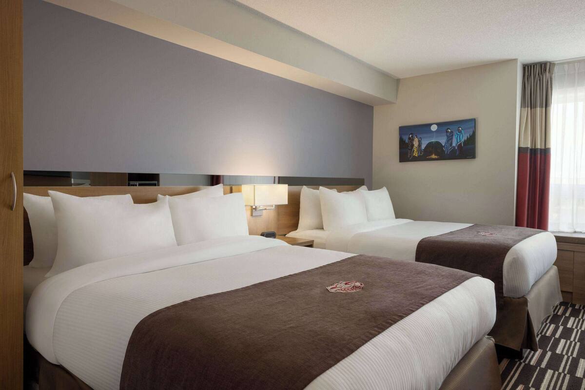 A hotel room with two beds, a painting on the wall, and a window with curtains.