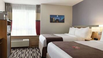 A hotel room with two beds, a desk, a chair, a heater, and a painting on the wall.