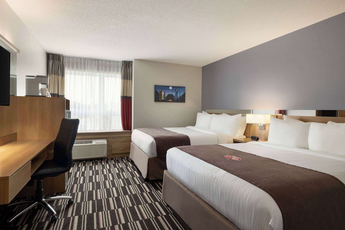 A hotel room with two beds, a desk, a chair, a TV, and a painting on the wall.