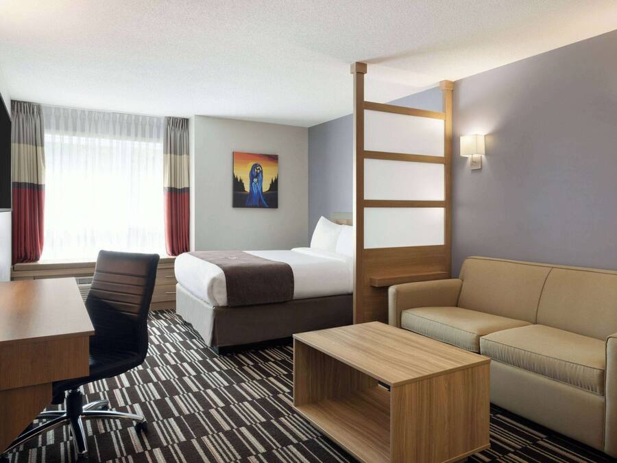 Een hotelkamer met een bed, een bank, een bureau, een stoel en een schilderij aan de muur.