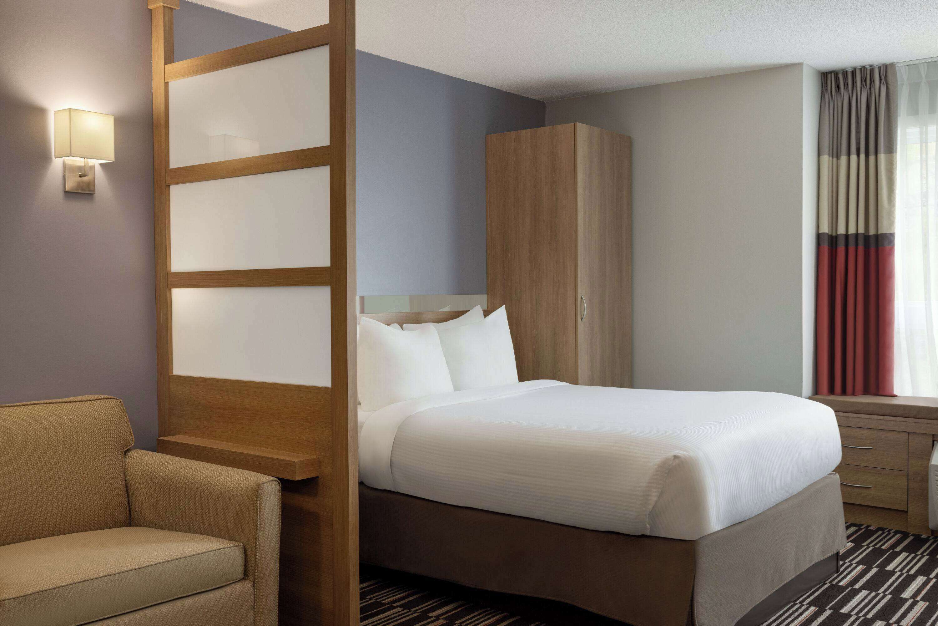 A hotel room with a bed, a wooden wardrobe, a sofa, and a window with curtains.