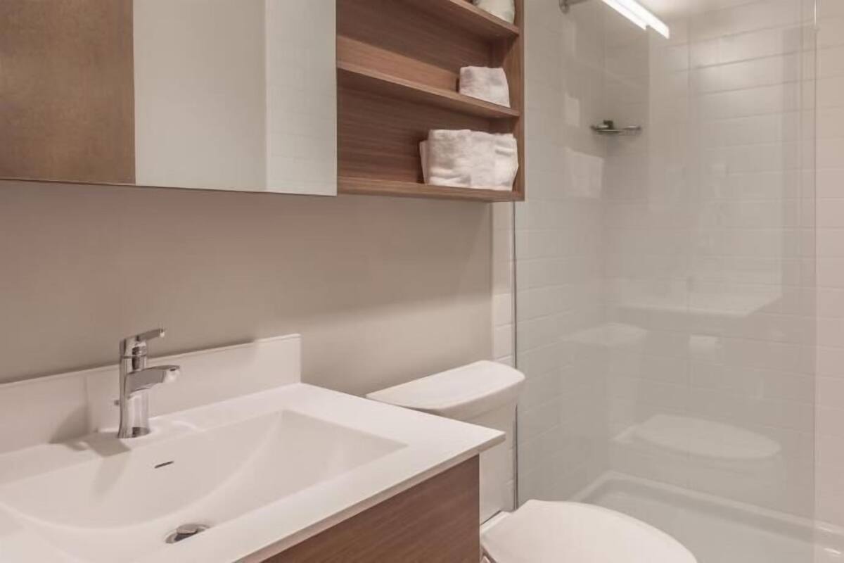 A modern bathroom with a white sink, wooden vanity, and a glass shower enclosure.
