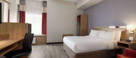 Een hotelkamer met een bed, een bureau, een stoel, een kledingkast en een raam met gordijnen.