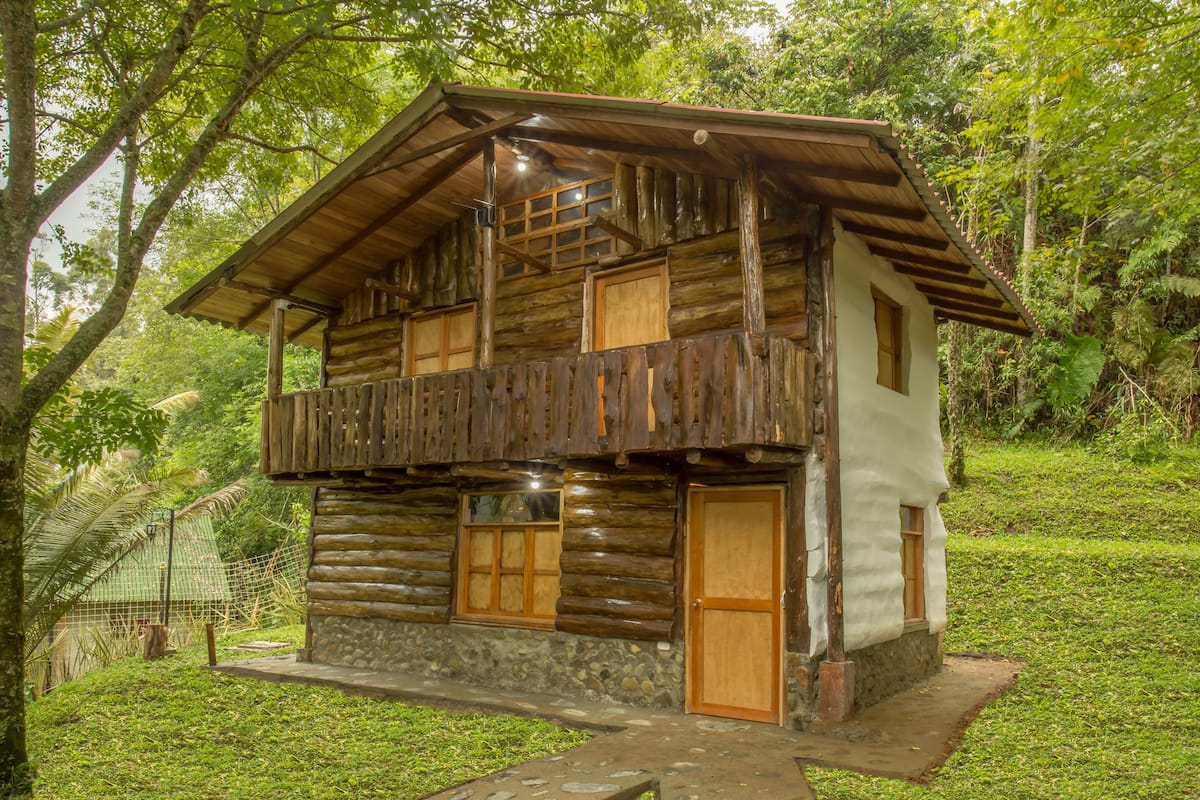A rustic log cabin with a balcony, a stone foundation, and a wooden door.