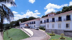 A building with a curved driveway, a white van parked in front, and well-maintained gardens with circular hedges. - JS Park Hotel (Sao Lourenco)