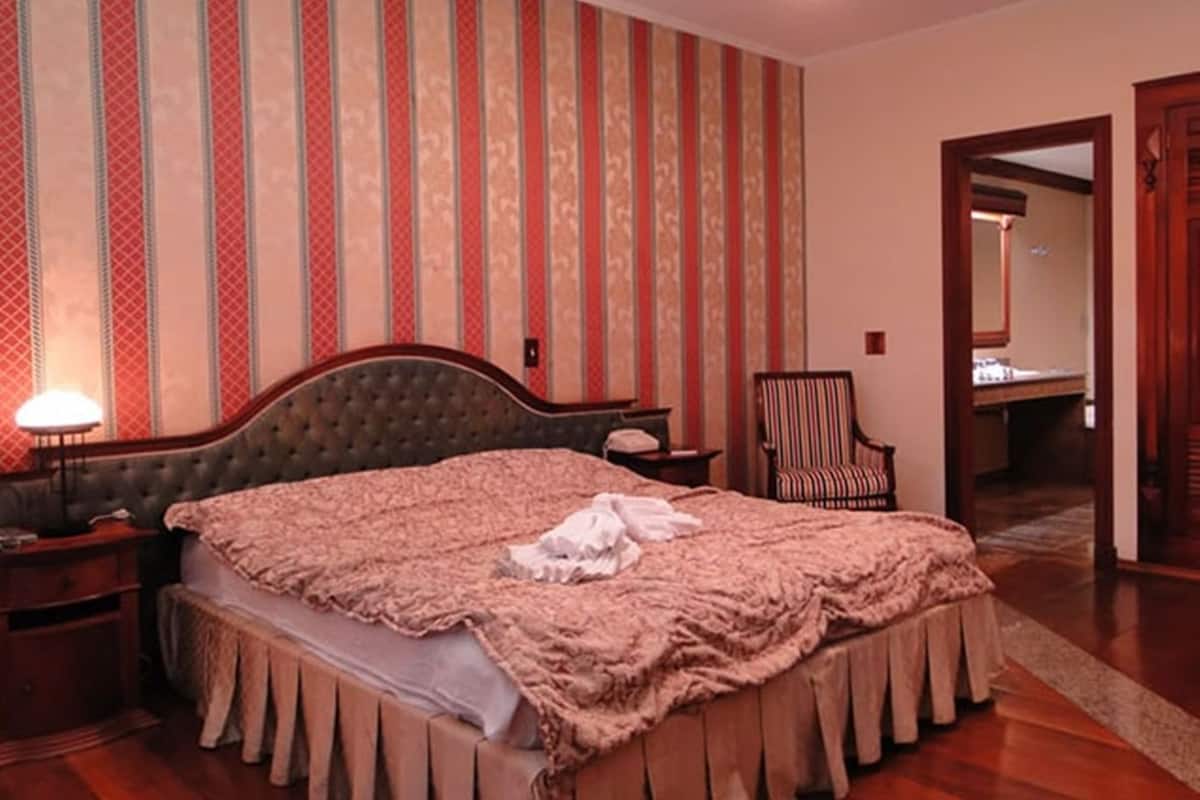 A bedroom with a large bed, a chair, a nightstand, and a mirror.