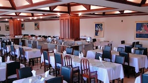 A dining area with multiple tables and chairs, a central buffet, and artwork on the walls. - JS Park Hotel (Sao Lourenco)