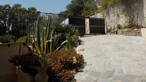 A stone pathway leading to a gated entrance with a decorative metal gate, surrounded by cacti and flowering plants. - Villa with pool and private Spa facing the sea (Conca)