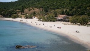 A beach with clear blue water, sandy shore, and a building with a red roof. - Villa with pool and private Spa facing the sea (Conca)