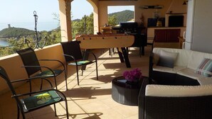 A terrace with outdoor seating, a foosball table, and a kitchen area with a view of the sea. - Villa with pool and private Spa facing the sea (Conca)